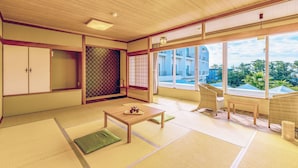 A traditional Japanese room with tatami flooring, a low table with a tray, a green cushion, and a view of a building through large windows.
