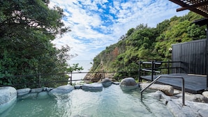 A hot spring area with a wooden deck, rocky edges, and a view of the sea.