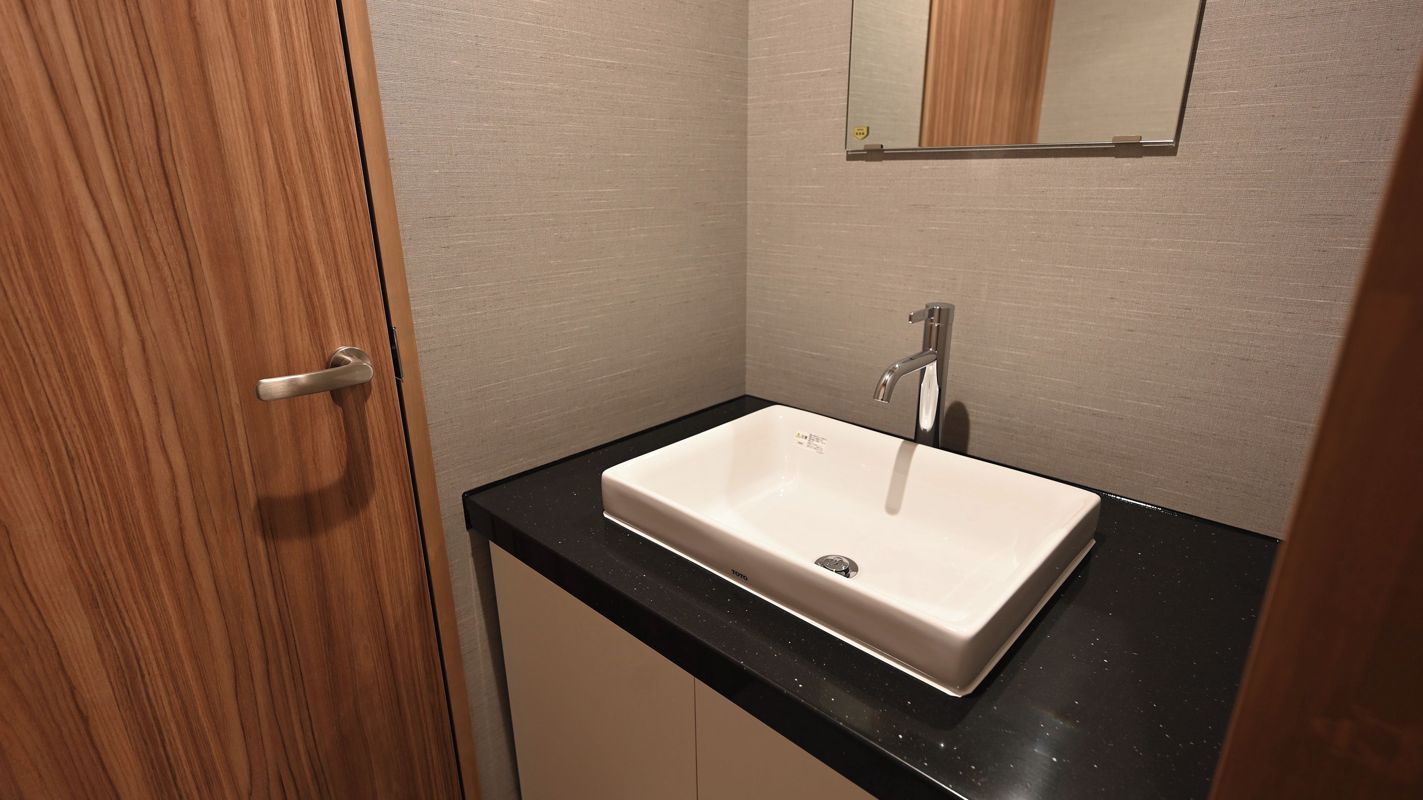 A bathroom with a white sink, a mirror above it, and a wooden door.