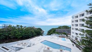 Piscina no terraço com vista para o mar, cercada por vegetação e edifícios modernos.