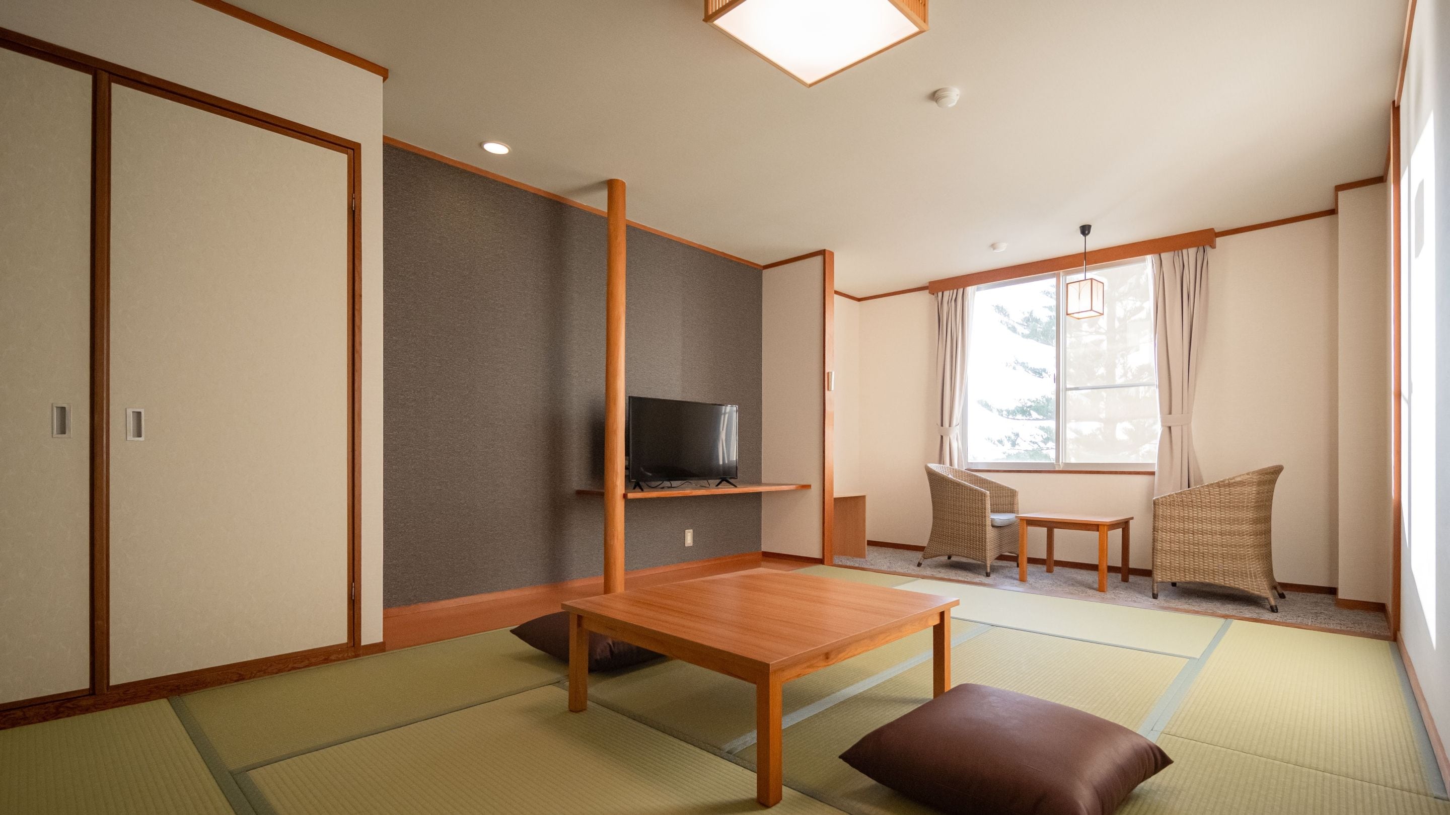 A traditional Japanese room with tatami flooring, a low wooden table, a television on a shelf, and a window with curtains.