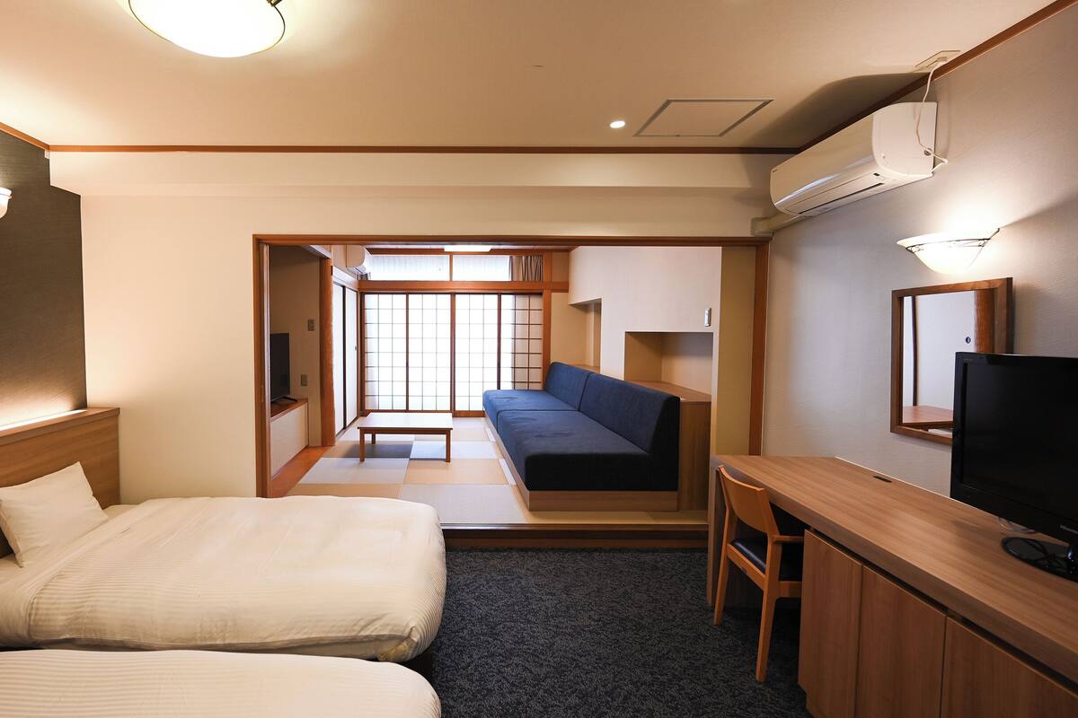 A hotel room with two beds, a sofa, a TV, and a desk.