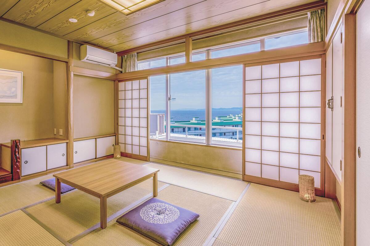 A traditional Japanese room with tatami flooring, a low wooden table, a cushioned bench, and a large shoji screen door.