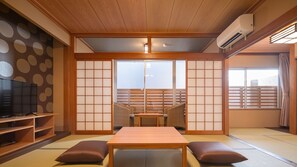 Una habitación japonesa tradicional con suelo de tatami, una mesa baja, cojines, un televisor y puertas correderas.