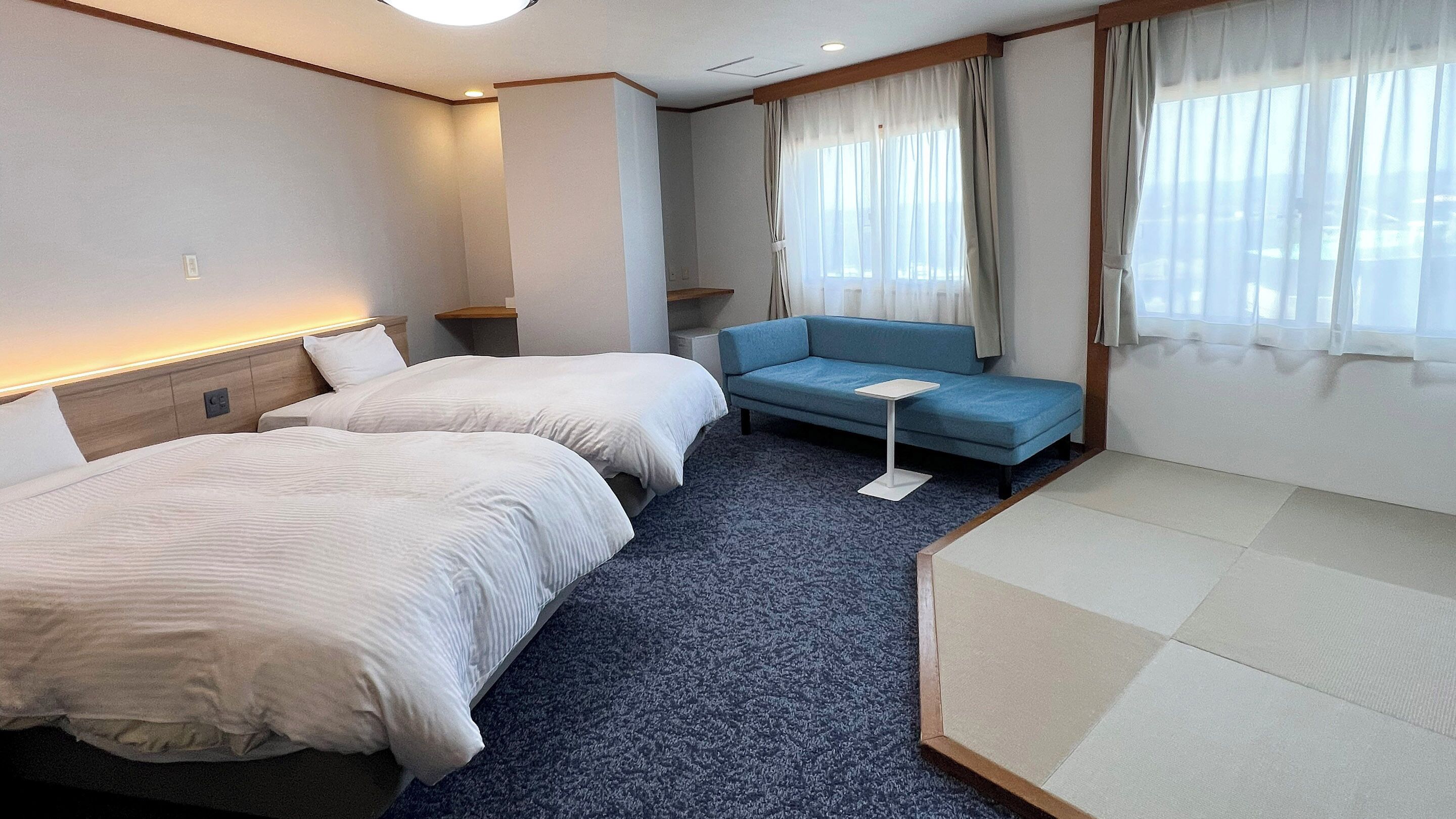 A hotel room with two beds, a sofa, a small table, and a window with curtains.