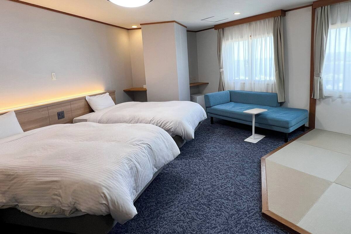 A hotel room with two beds, a sofa, a small table, and a window with curtains.