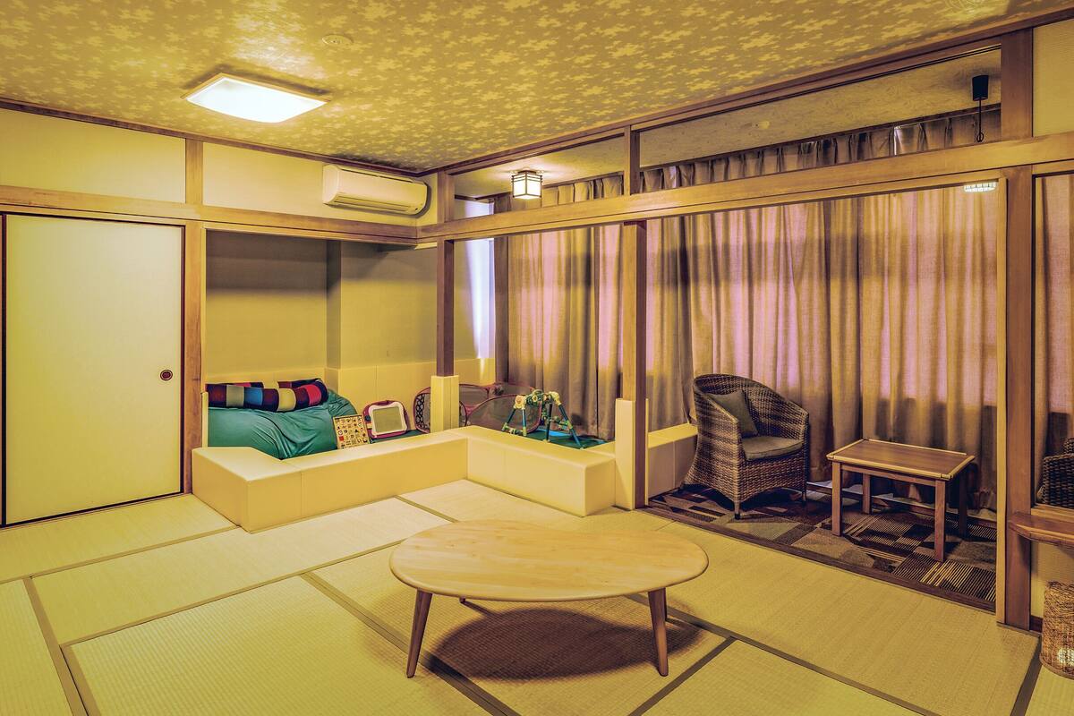 A traditional Japanese-style room with tatami flooring, a low table, a cushioned seating area, and a wicker chair.