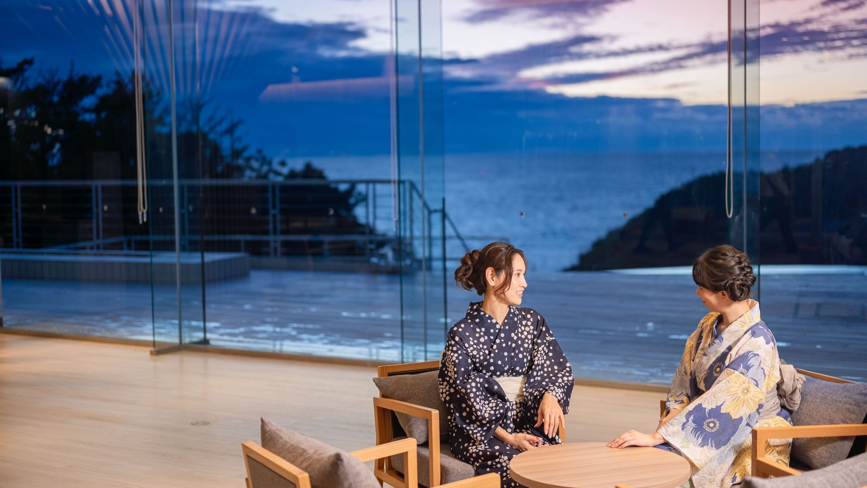 Dos personas sentadas en una mesa redonda con vista al mar a través de amplios ventanales.