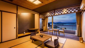 Una habitación japonesa tradicional con suelo de tatami, una mesa baja con juego de té y un balcón con vistas al mar y a las montañas.