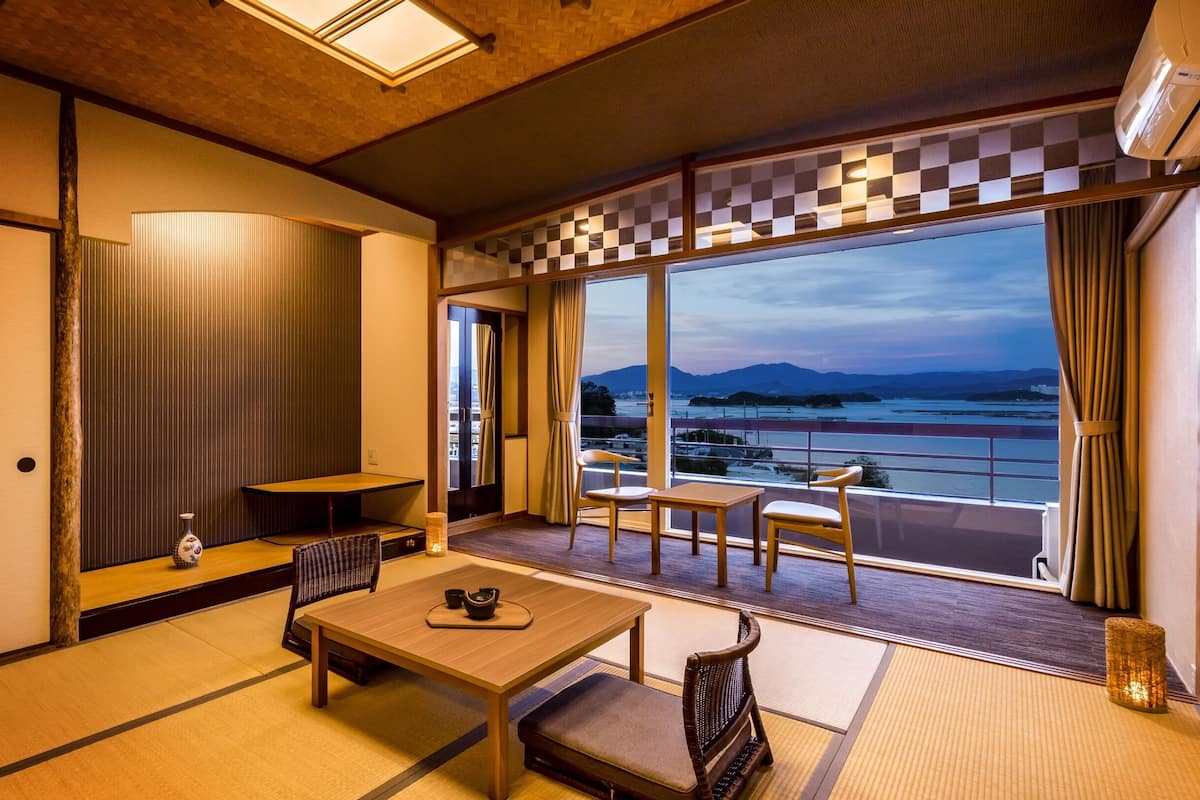 Een traditionele Japanse kamer met tatami vloeren, een lage tafel met een theeset, en een balkon met uitzicht op zee en bergen.