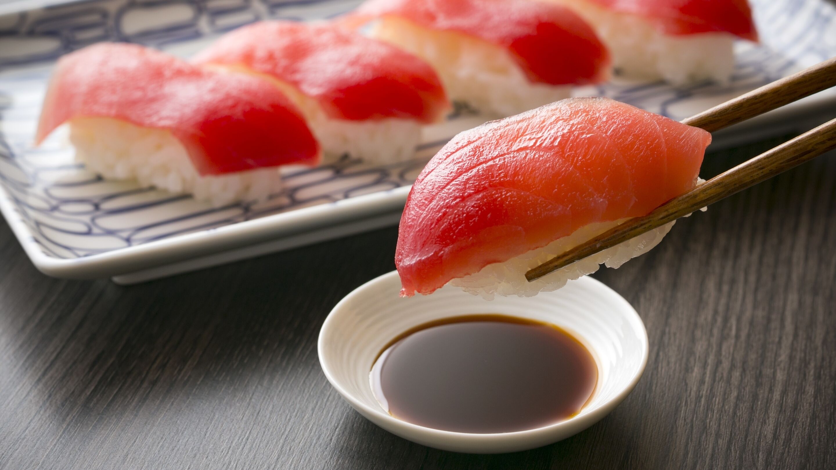 Des sushis présentés sur une assiette, accompagnés de baguettes et d’un petit bol de sauce soja.