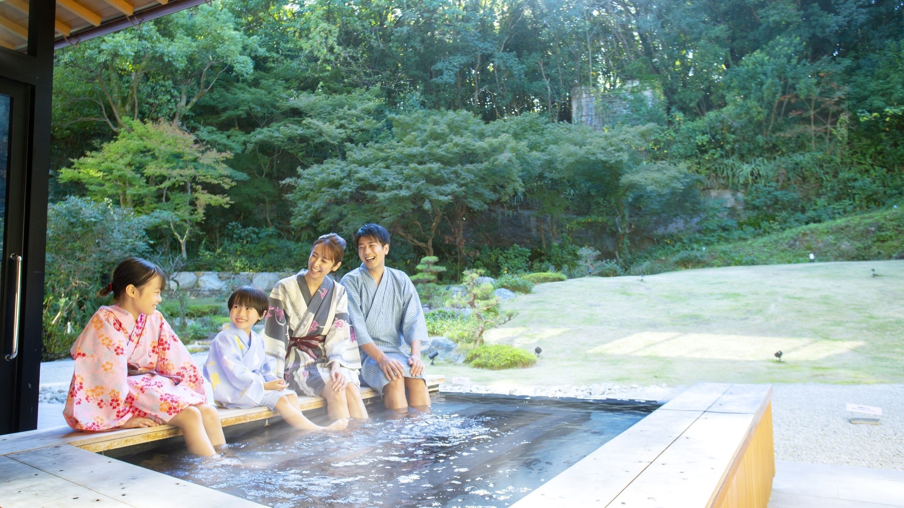 A group of people sitting in a hot spring bath outdoors surrounded by greenery.