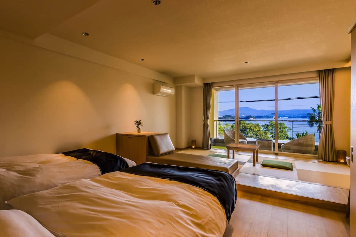 Een hotelkamer met twee bedden, een tafeltje, een stoel en uitzicht op een meer en bergen.