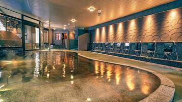 A modern indoor pool with a wet floor, a stone wall, and a series of showerheads.