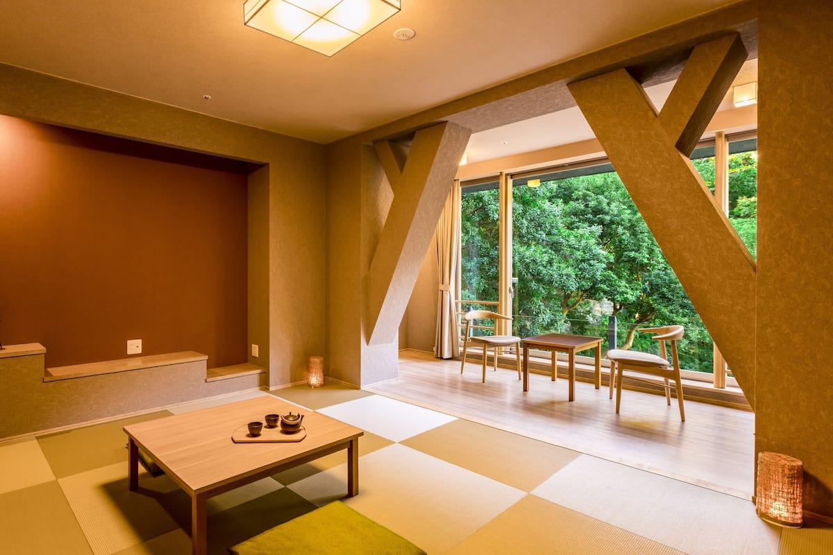 Een modern interieur met een houten tafel, tatami matten en uitzicht op groen door grote ramen.