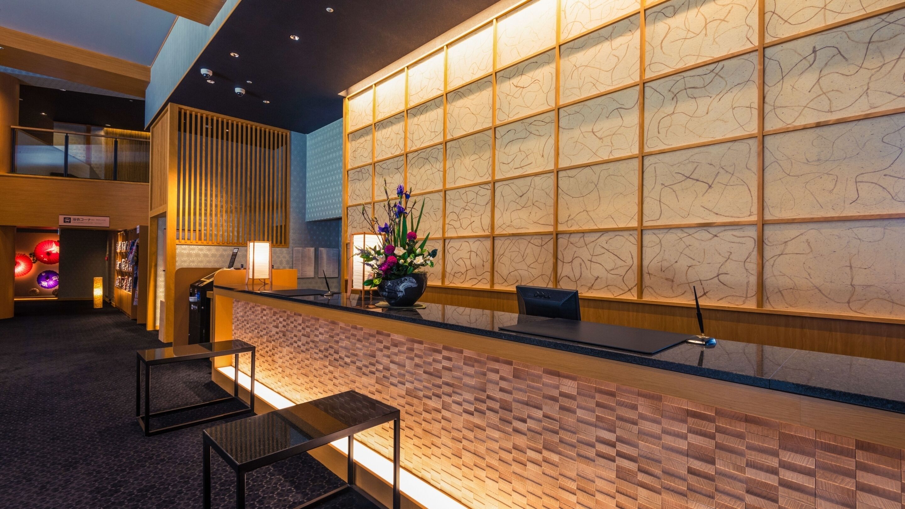 A reception desk with a check-in counter, a seating area with chairs, a decorative wall with a pattern, and a ceiling with recessed lighting.