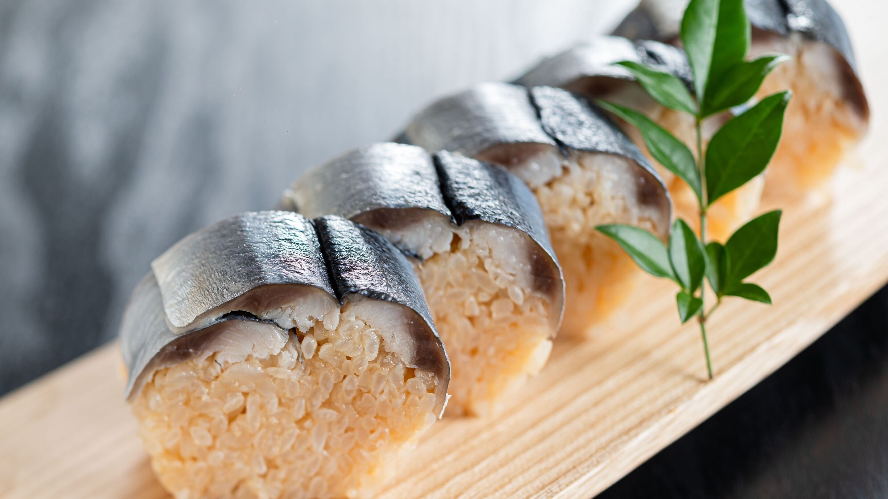 Una tabla de madera con rollitos de sushi cubiertos de rebanadas de pescado.