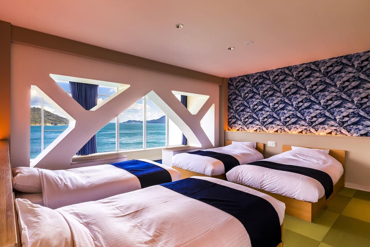 Ein Hotelzimmer mit zwei Betten, einem großen Fenster mit Meerblick und einer Wand mit Muster.