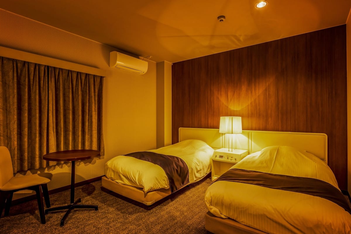 Ein Hotelzimmer mit zwei Betten, einem Schreibtisch, einem Stuhl, einer Klimaanlage und einer Lampe.
