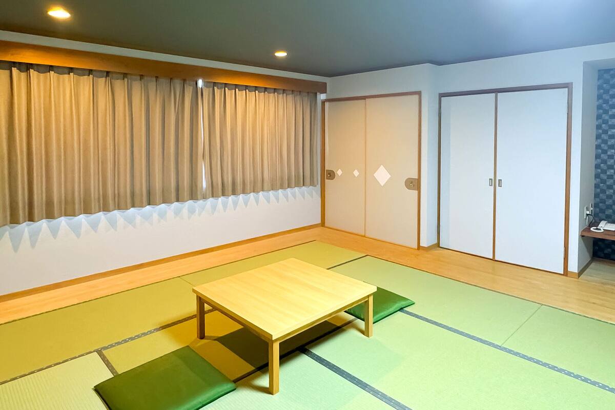 Ein Zimmer mit Tatami-Matten, einem Holztisch, einem Fernseher auf einem Schrank und Schiebetüren.