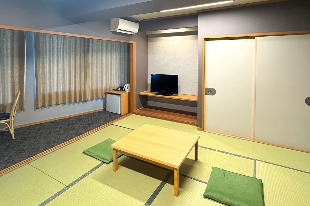 Ein Zimmer mit Tatami-Boden, einem niedrigen Tisch, einem Stuhl, einem Fernseher und einem Kleiderschrank.