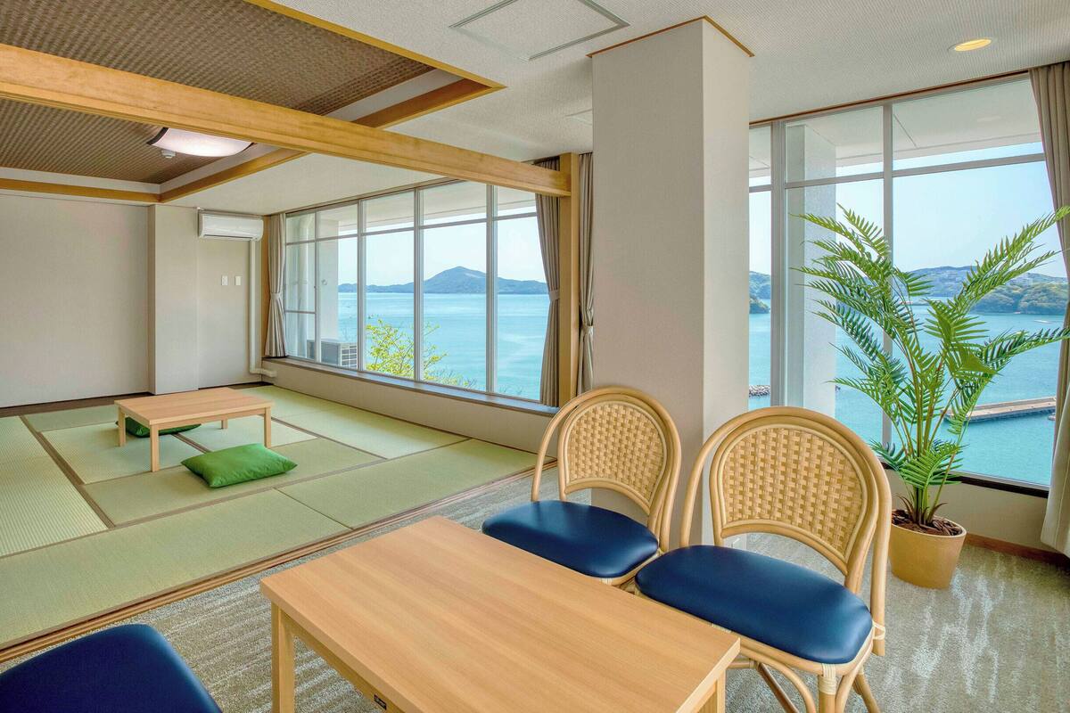 Ein traditioneller Raum mit Tatami-Matten und Meerblick, ein Holztisch und zwei Stühle.