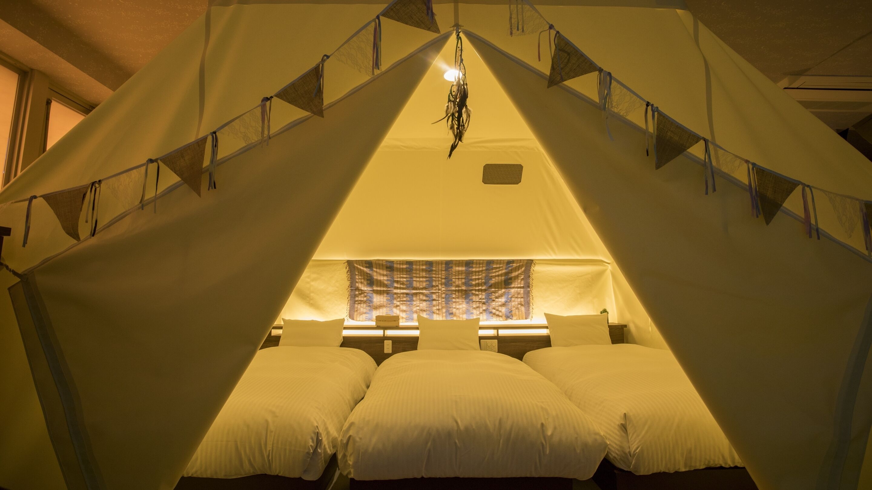 Quarto com tenda, uma cama, uma luminária pendente e uma janela com cortinas.