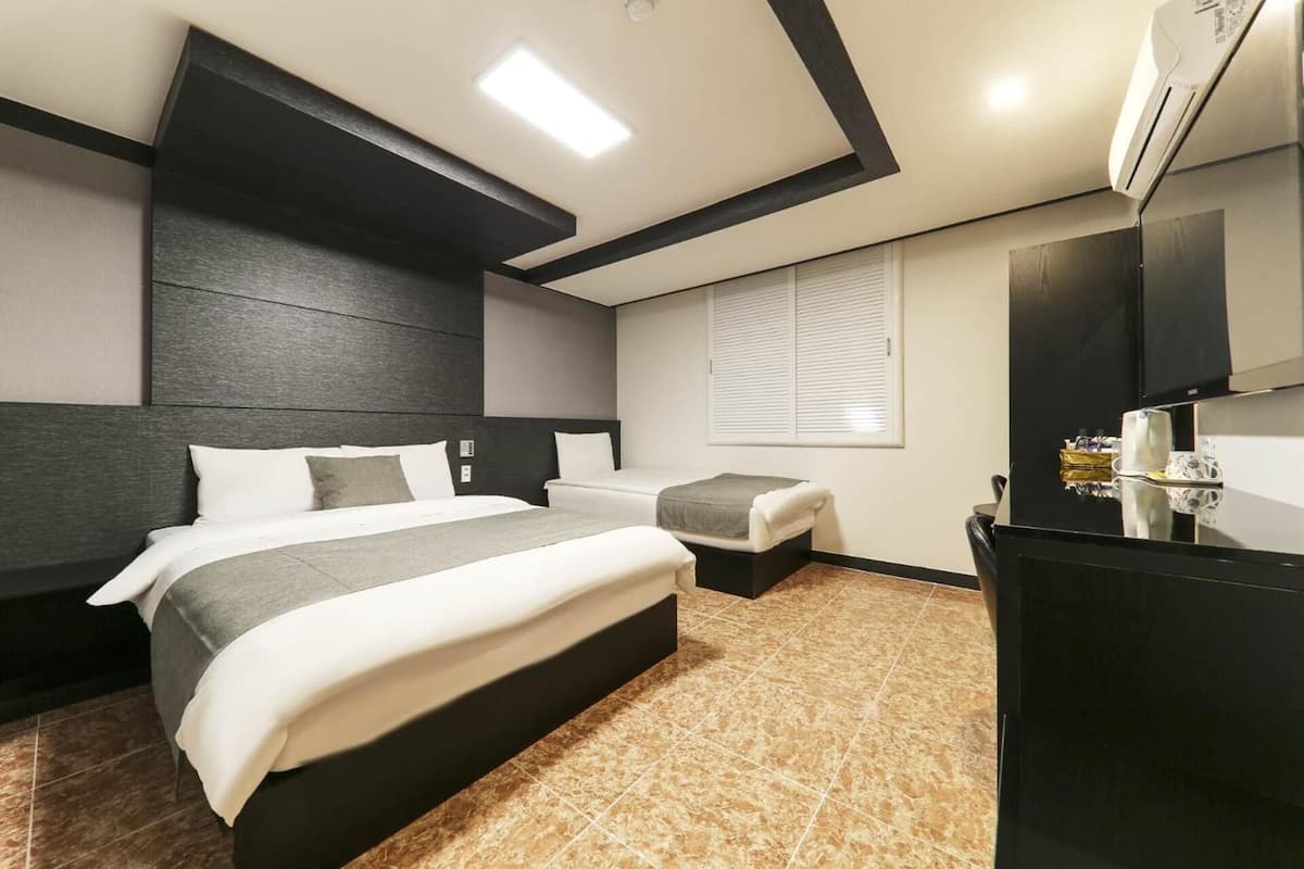 A modern hotel room with a large bed, a smaller bed, a desk, and a TV.