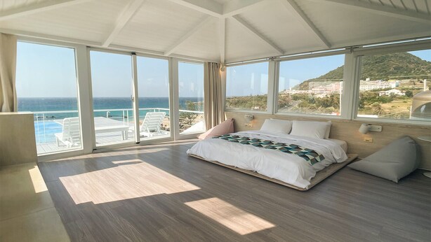 Un dormitorio amplio con una cama grande, vistas al mar y un balcón con mobiliario de exterior.