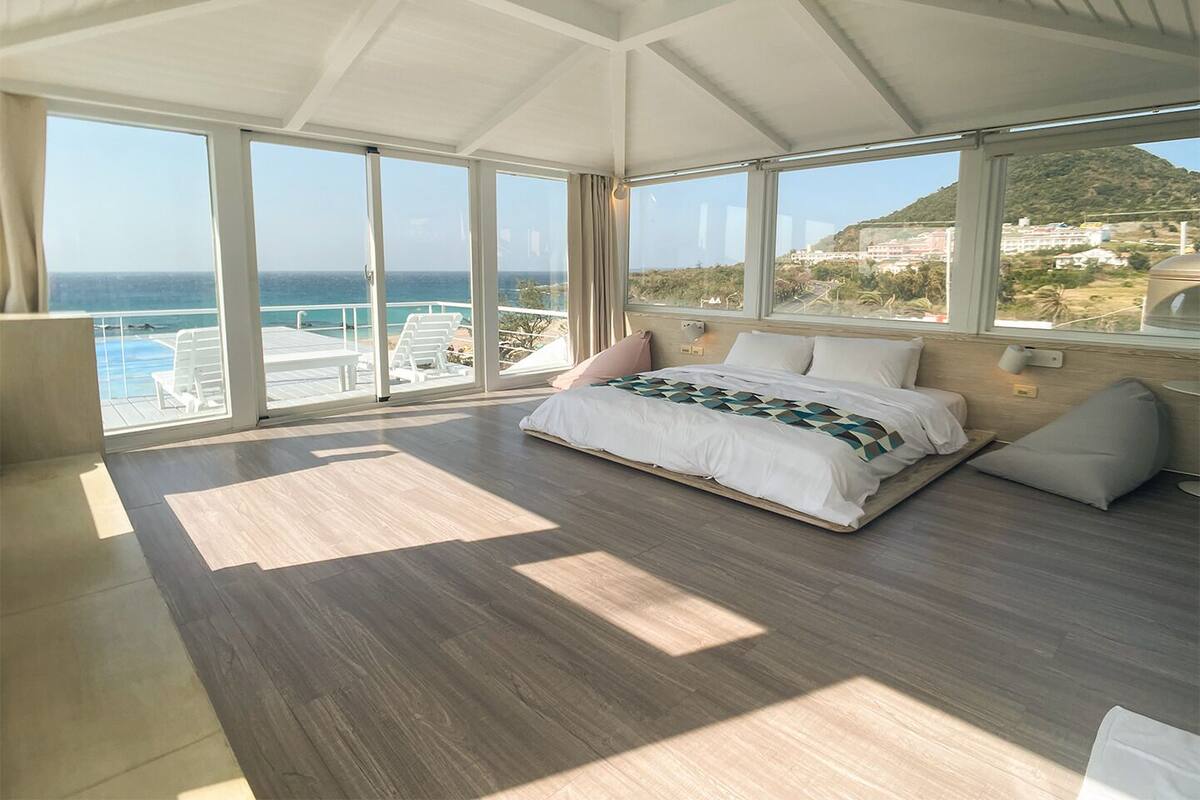 Ein geräumiges Schlafzimmer mit einem großen Bett, Meerblick und einem Balkon mit Sitzgelegenheit.