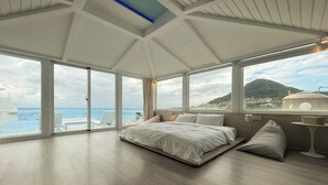 Un dormitorio amplio con una cama grande, una mesita de noche y vistas al mar y a la montaña.