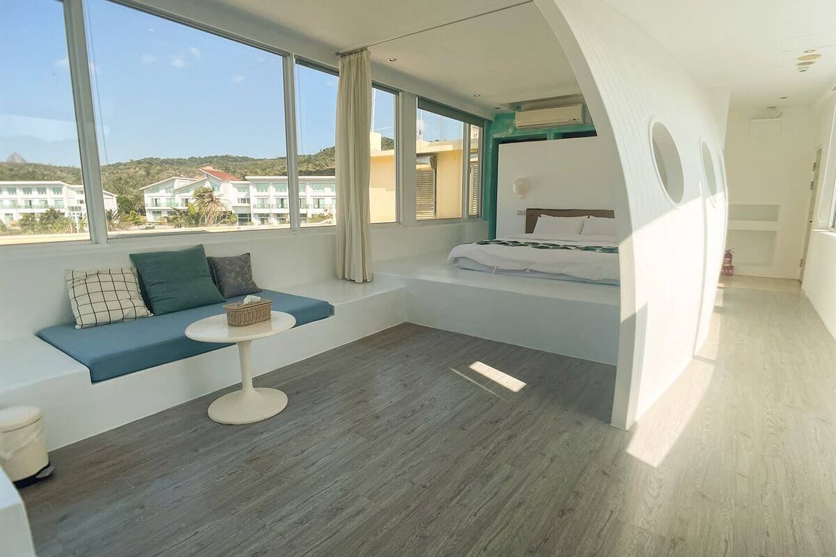Ein modernes Schlafzimmer mit integriertem Bett, einer Sitzecke mit Tisch und großen Fenstern mit Blick auf Gebäude und Hügel.
