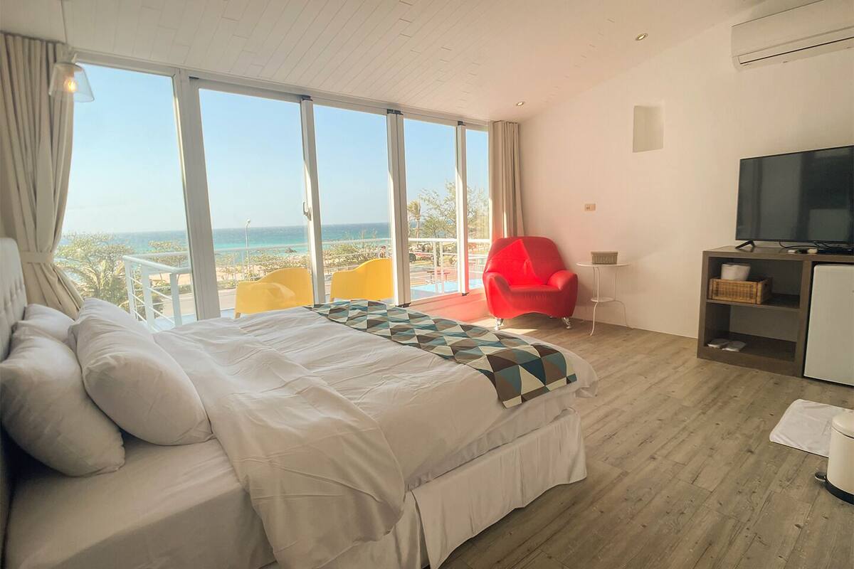 Ein Schlafzimmer mit einem Bett, einem roten Sessel, einem Fernseher und Meerblick.