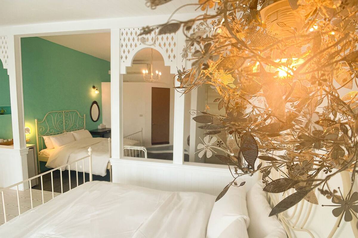 Ein Schlafzimmer mit einem weißen Bett, einer grünen Wand und einer Zimmerpflanze in der Ecke.