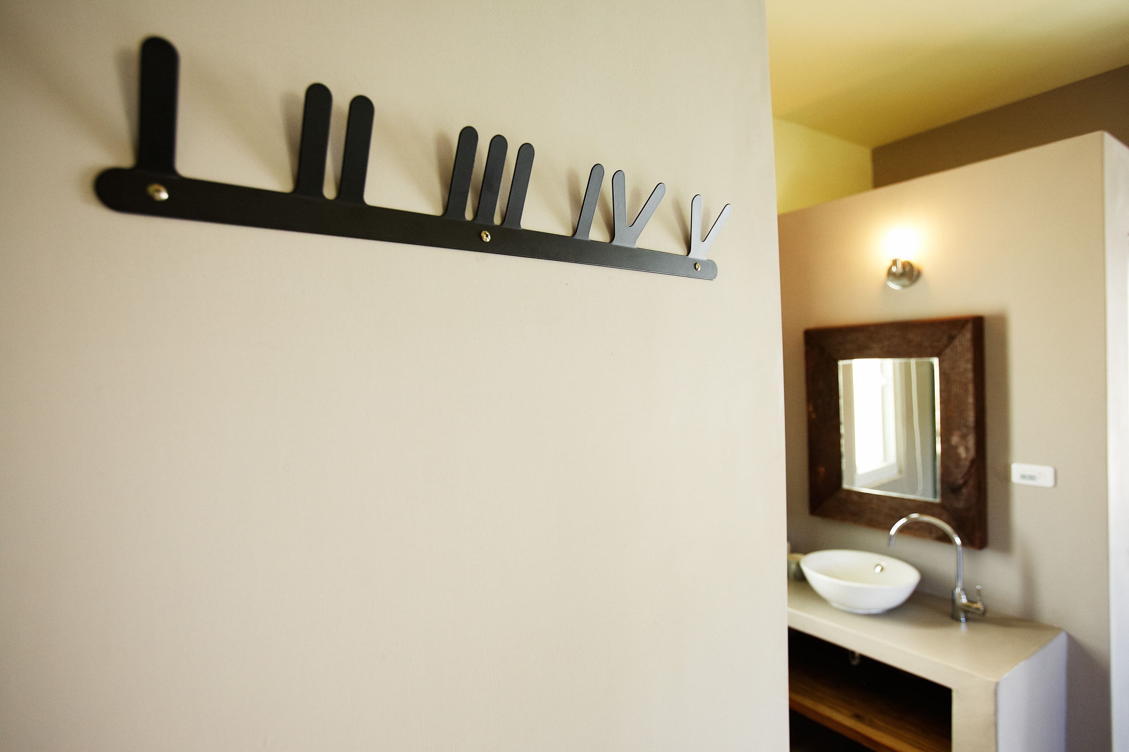 A bathroom with a white sink, a mirror, and a black wall-mounted rack with multiple hooks.