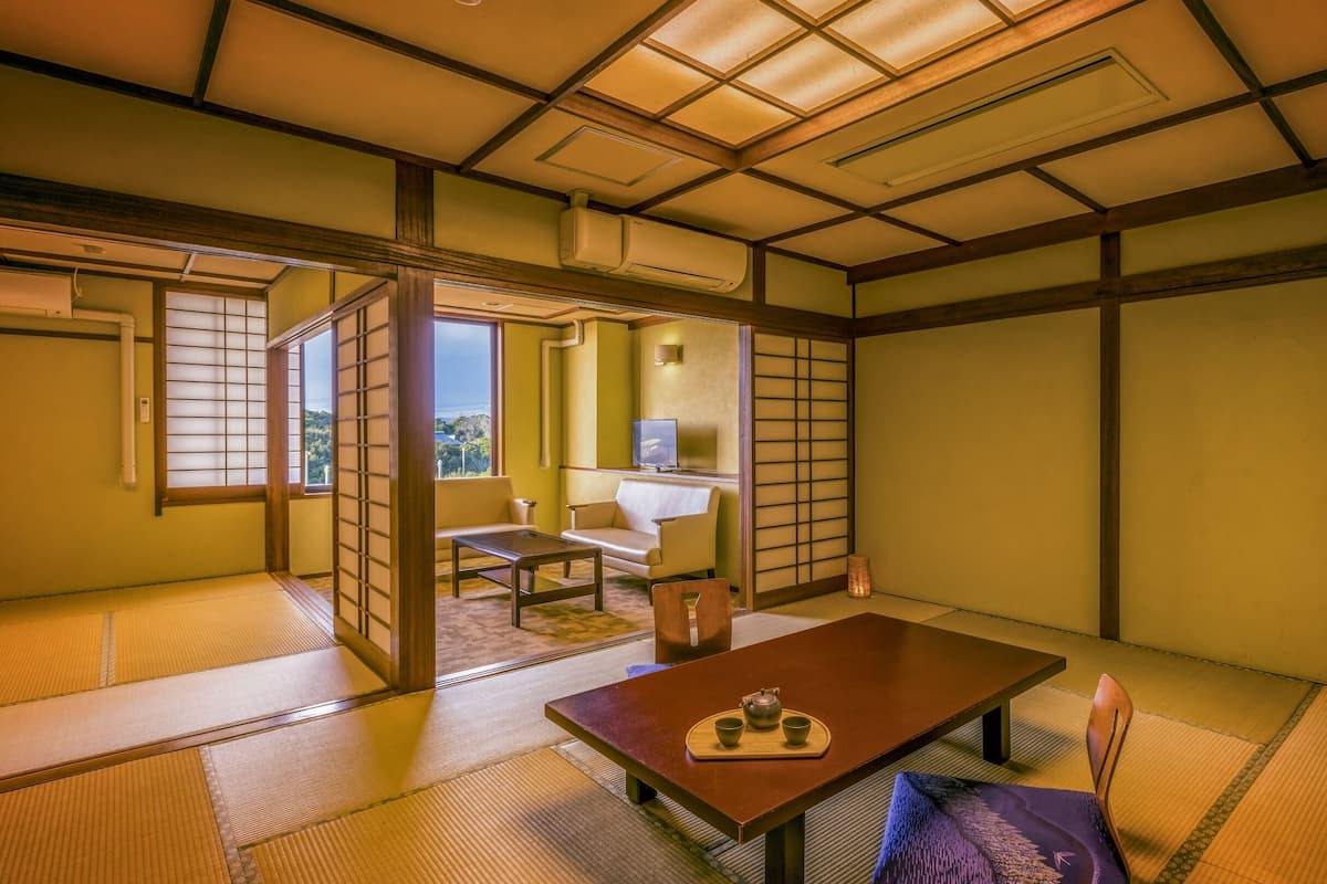 Ein traditioneller japanischer Raum mit Tatami-Boden, einem niedrigen Tisch mit Teeservice, einer Sitzecke und einer Schiebetür zu einem Balkon.