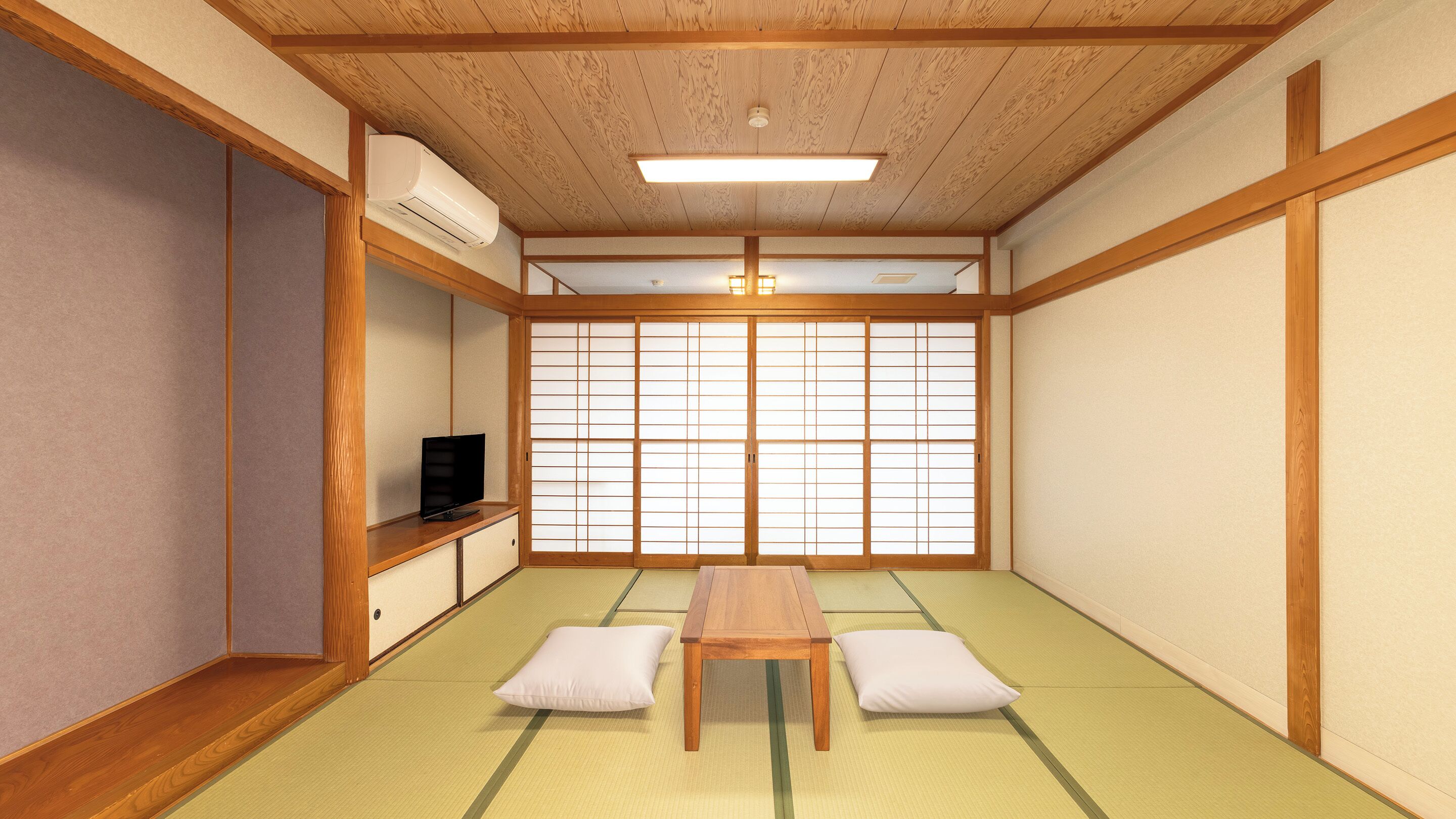 Una habitación de tatami con una mesa baja, cojines, un televisor sobre una estantería y puertas correderas shoji.