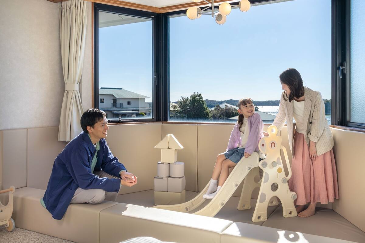 Ein Zimmer mit großen Fenstern, einer Couch, einer Spielecke mit Rutsche und einer Lampe.