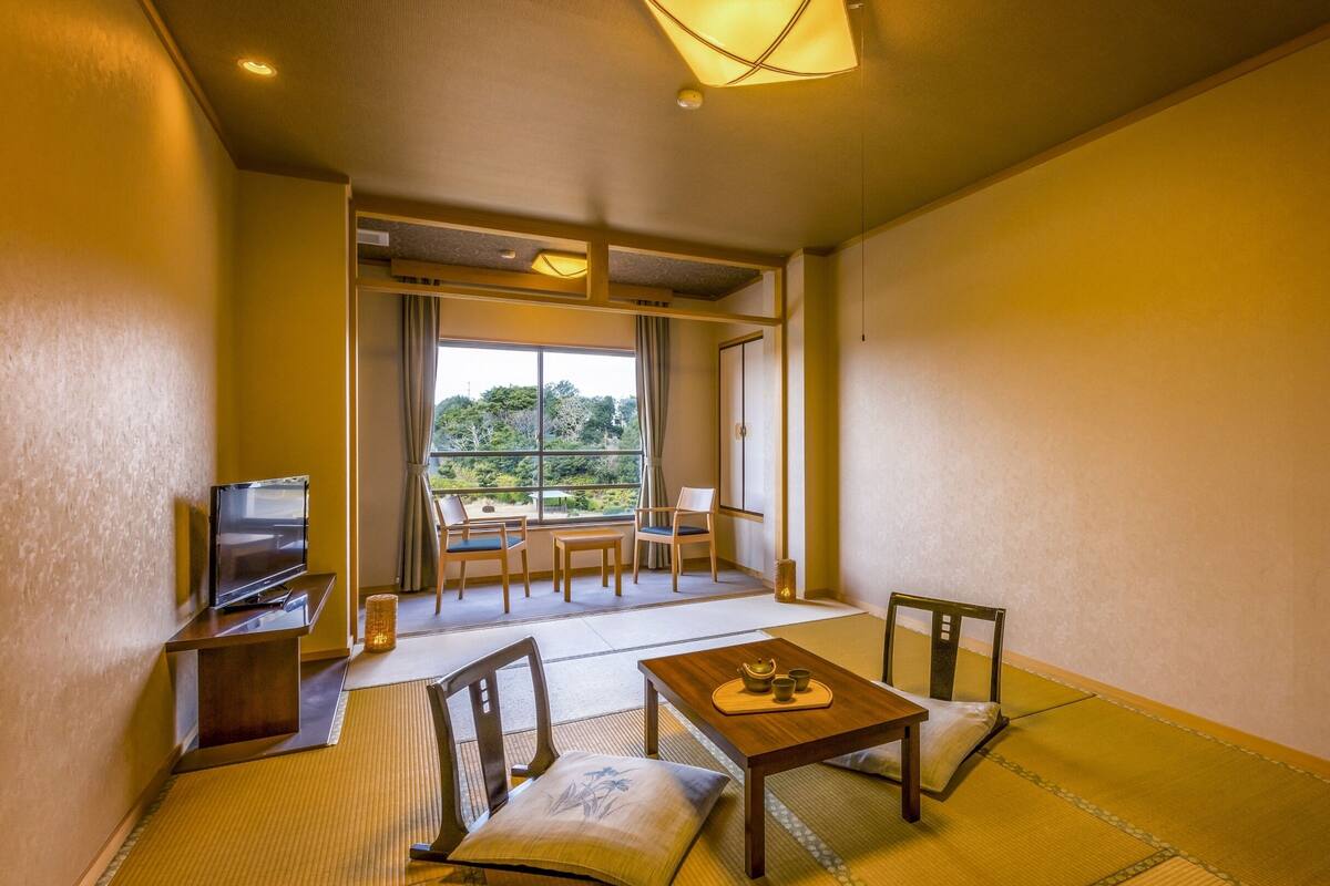 Ein traditioneller japanischer Raum mit Tatami-Böden, einem niedrigen Tisch mit Teeservice und einem Fernseher auf einem Holzboden.
