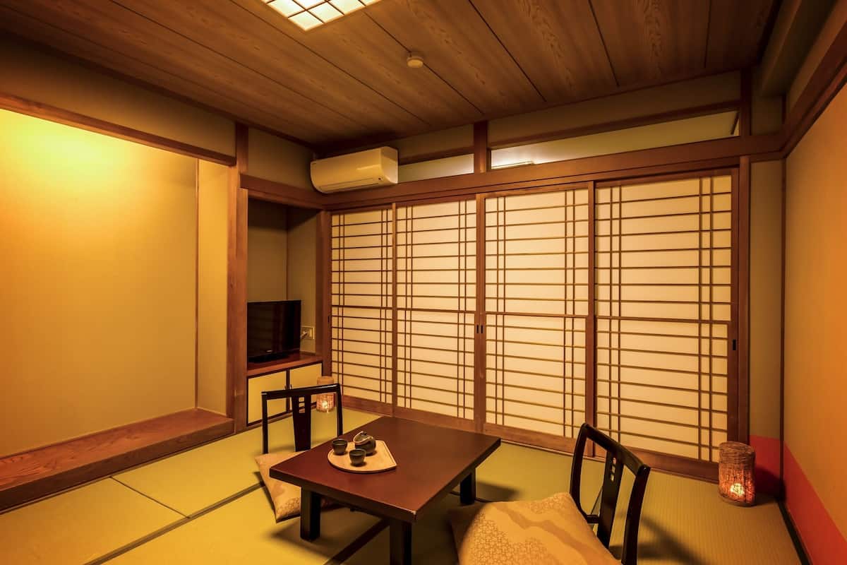 Ein traditioneller japanischer Raum mit Tatami-Boden, einem niedrigen Tisch mit Kissen, einem Fernseher und verschiebbaren Shoji-Türen.