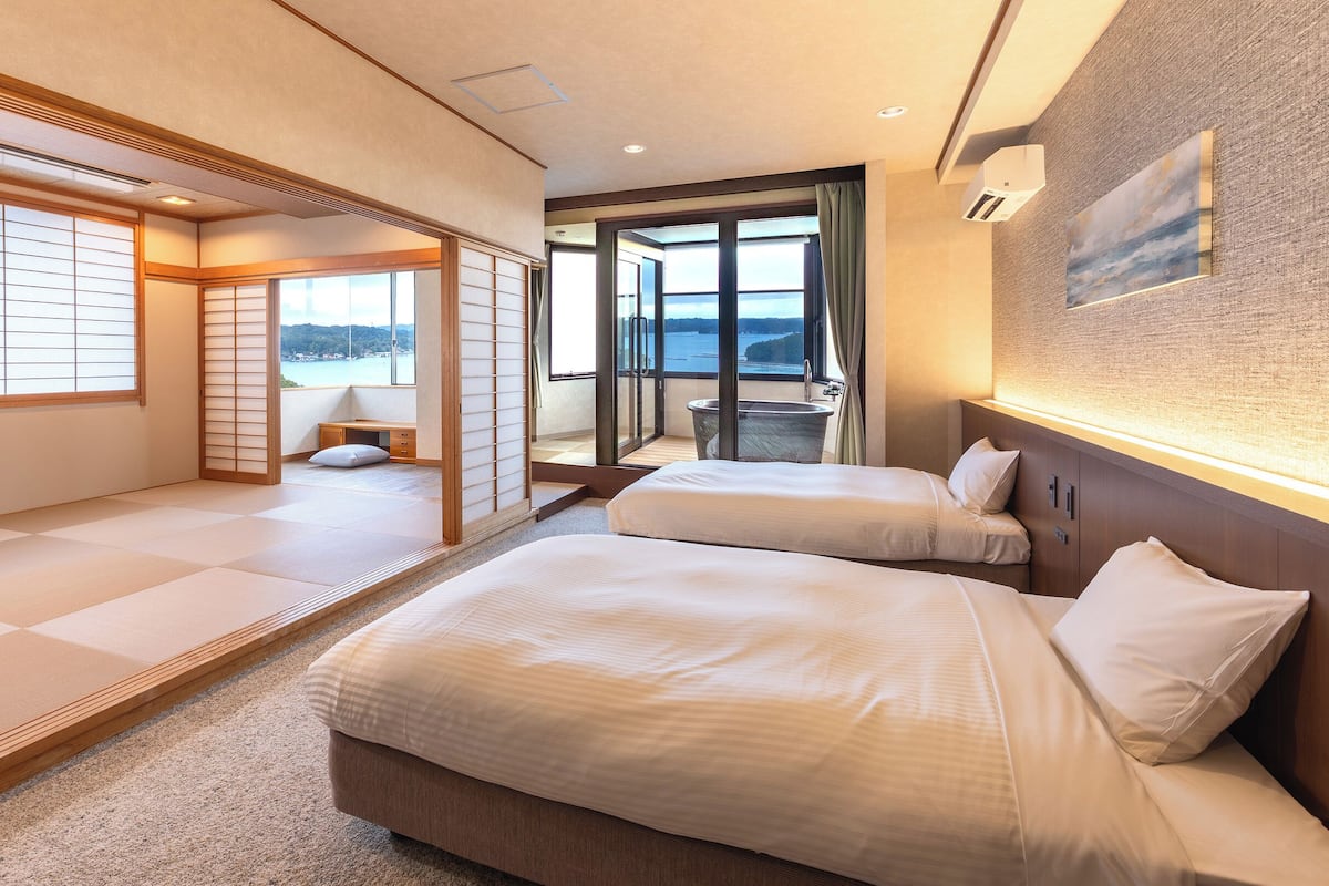 Ein Hotelzimmer mit Tatami-Böden, zwei Betten, einer Schiebetür zu einem Balkon und Meerblick.