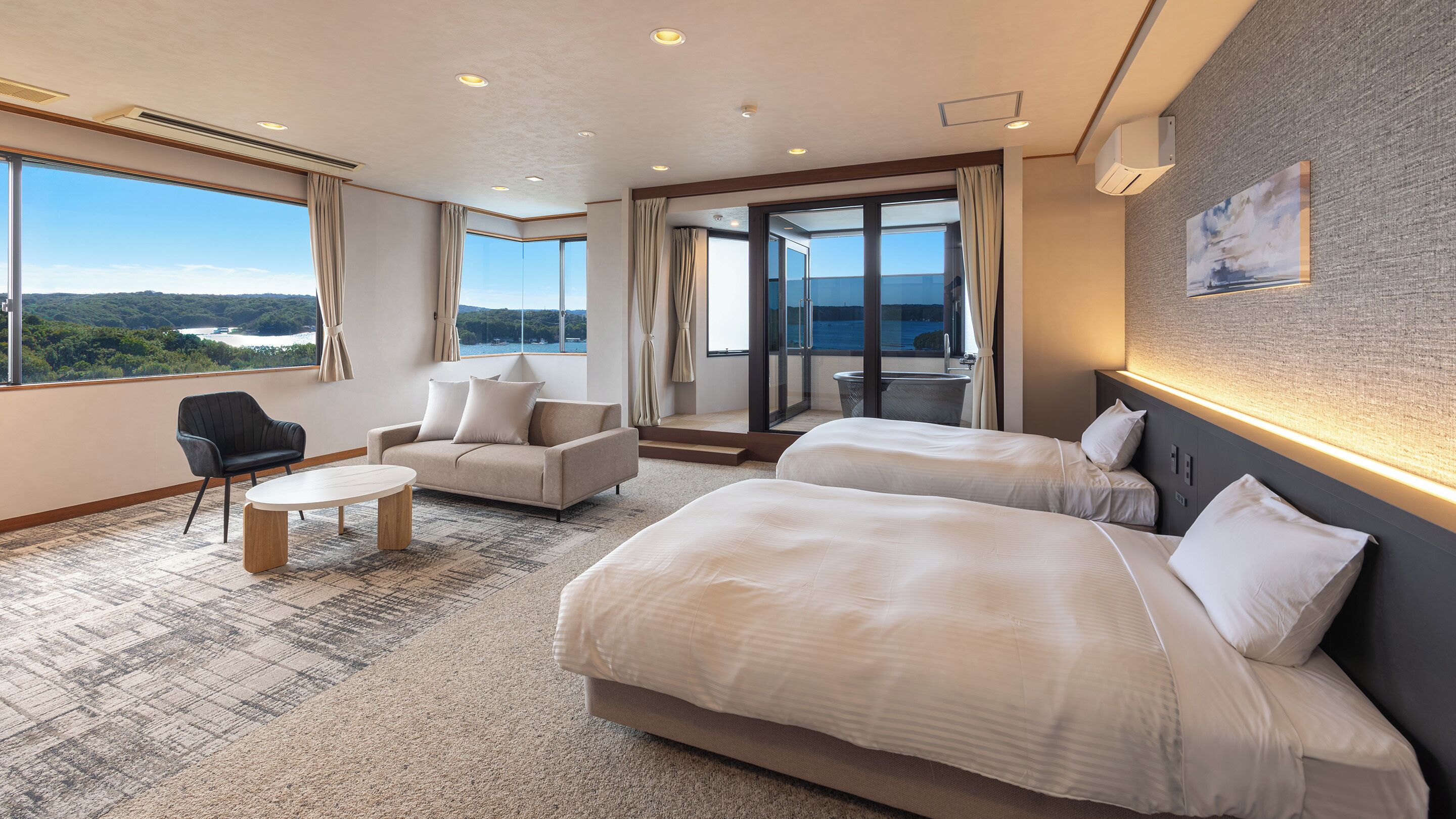 Quarto de hotel com duas camas, um sofá, uma mesinha e vista para o exterior.