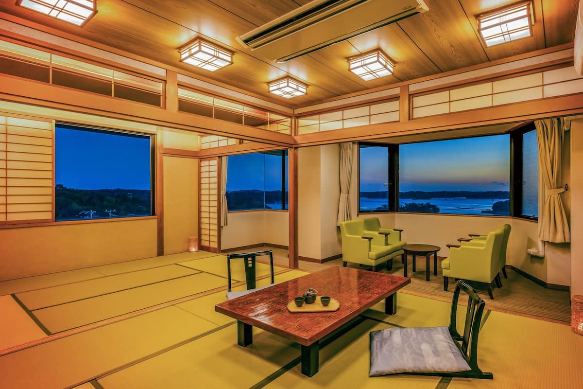 Ein traditioneller japanischer Raum mit Tatami-Böden, einem niedrigen Tisch mit Teeservice und großen Fenstern mit Blick auf das Meer.