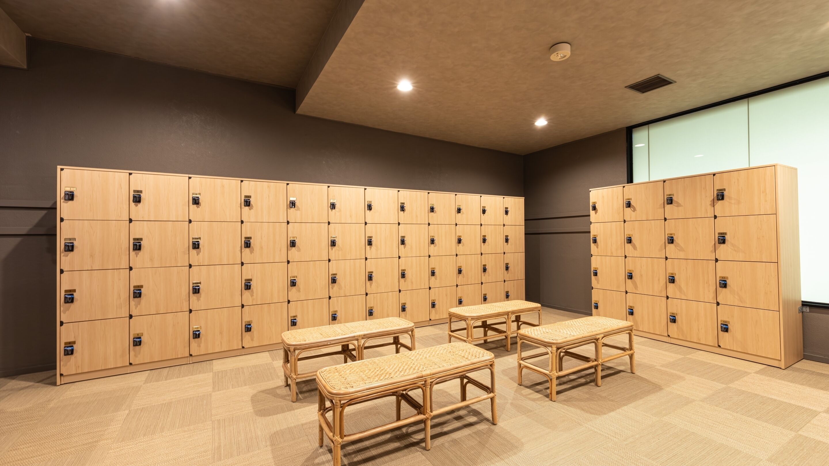 A locker room with multiple wooden lockers, woven benches, and a carpeted floor.
