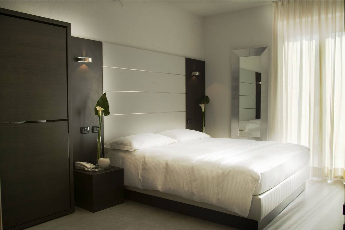 Une chambre à coucher moderne avec un grand lit, une table de chevet, un téléphone, un miroir et une armoire.