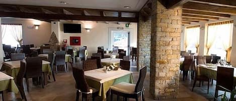 Een restaurant met meerdere tafels en stoelen, stenen zuilen en een houten plafond.