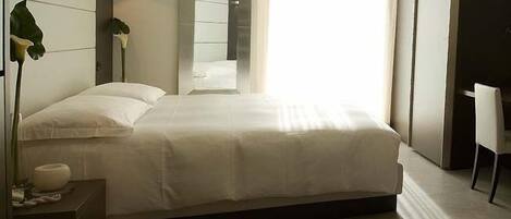 Una cama bien hecha en una habitación de hotel, con una mesita de noche, una silla y un espejo grande.