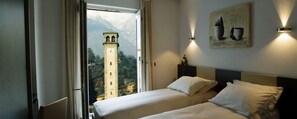 Habitación de hotel con dos camas, un ventanal con vistas a la montaña y una torre del reloj visible desde el exterior.