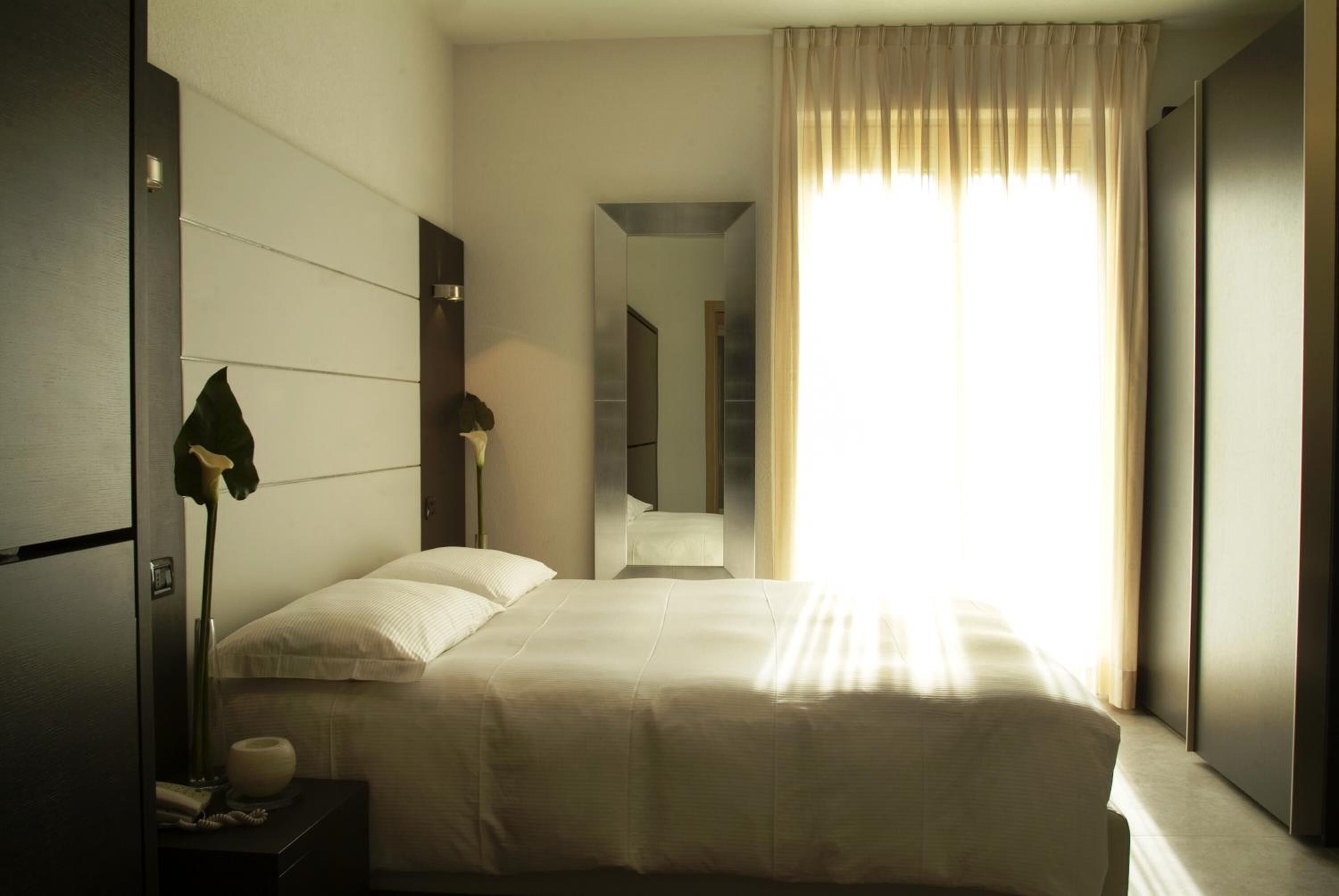Ein modernes Hotelzimmer mit einem großen Bett, einer Nachttischlampe, einem Spiegel und Blick auf den Flur.