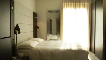 Ein modernes Hotelzimmer mit einem großen Bett, einer Nachttischlampe, einem Spiegel und Blick auf den Flur.